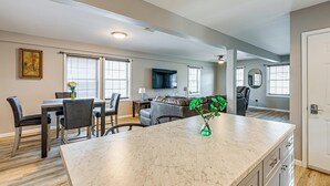 A modern kitchen with a marble countertop, dining area with chairs, a sofa, and a TV mounted on the wall. - Walkable Stay Near Hudson River, Dining & Shopping (Hudson)