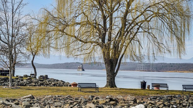 A lakeside park with benches, a large tree, and a distant lighthouse. - Walkable Stay Near Hudson River, Dining & Shopping (Hudson)