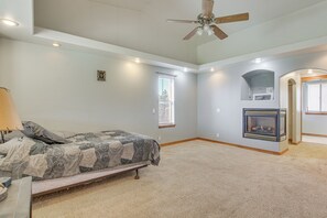 A bedroom with a bed, a ceiling fan, a fireplace, and a window.