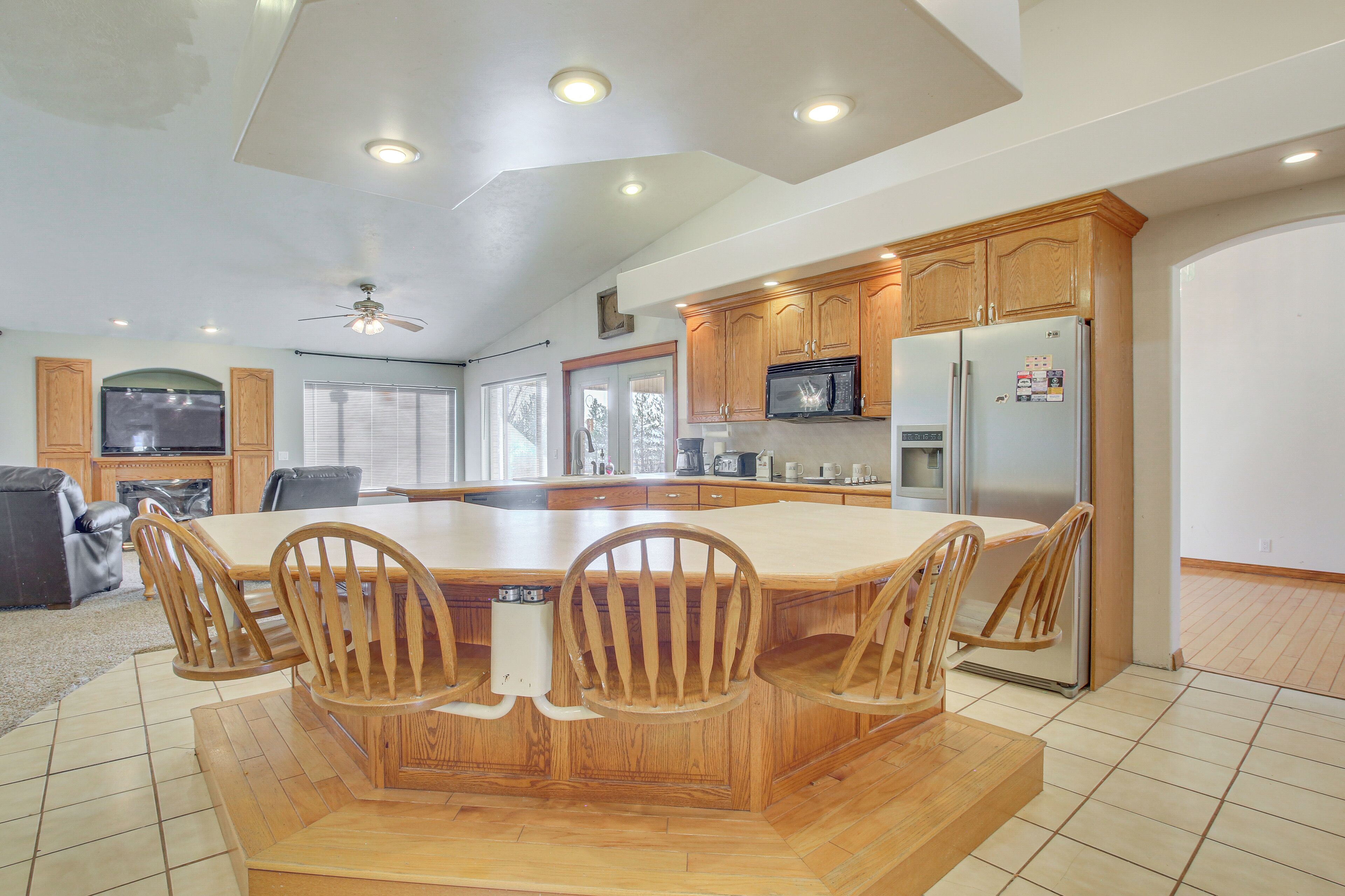 A spacious kitchen with wooden cabinets, a large island with chairs, a refrigerator, and a microwave.