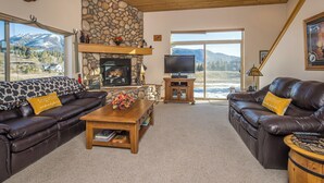 A cozy living room with leather sofas, a fireplace, a television, and a view of mountains.