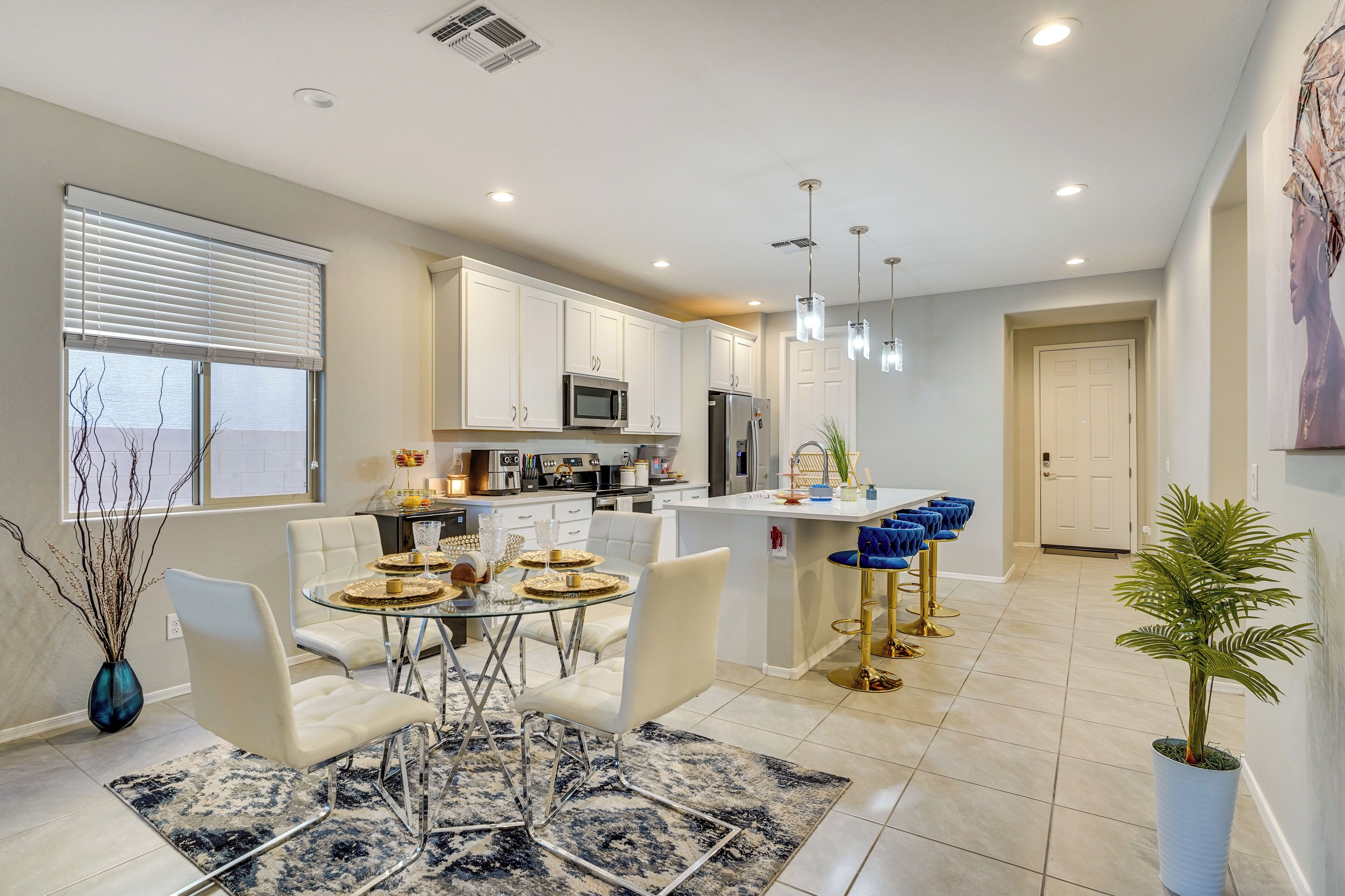 A modern kitchen with white cabinets, a central island, and a dining area with white chairs and a glass table.