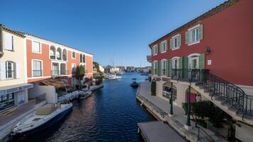 A canal with boats docked on the left, buildings with balconies on the right, and a clear blue sky above.