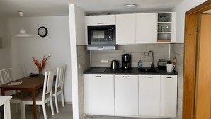Une cuisine de taille réduite avec des meubles blancs, un micro-ondes noir, une machine à café et un évier.