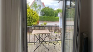 Un balcon avec une table et des chaises, une vue sur une maison et une haie.
