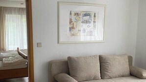 Une pièce avec un canapé beige, une carte encadrée accrochée au mur, une porte en bois et un luminaire blanc au plafond.