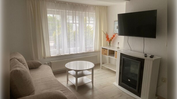Un salon avec un canapé, une table blanche, une cheminée et un téléviseur fixé au mur.