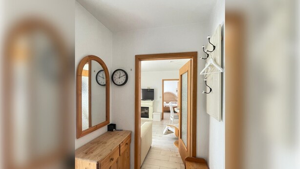 A hallway with wooden flooring, a wooden bench, a mirror, and a coat rack.