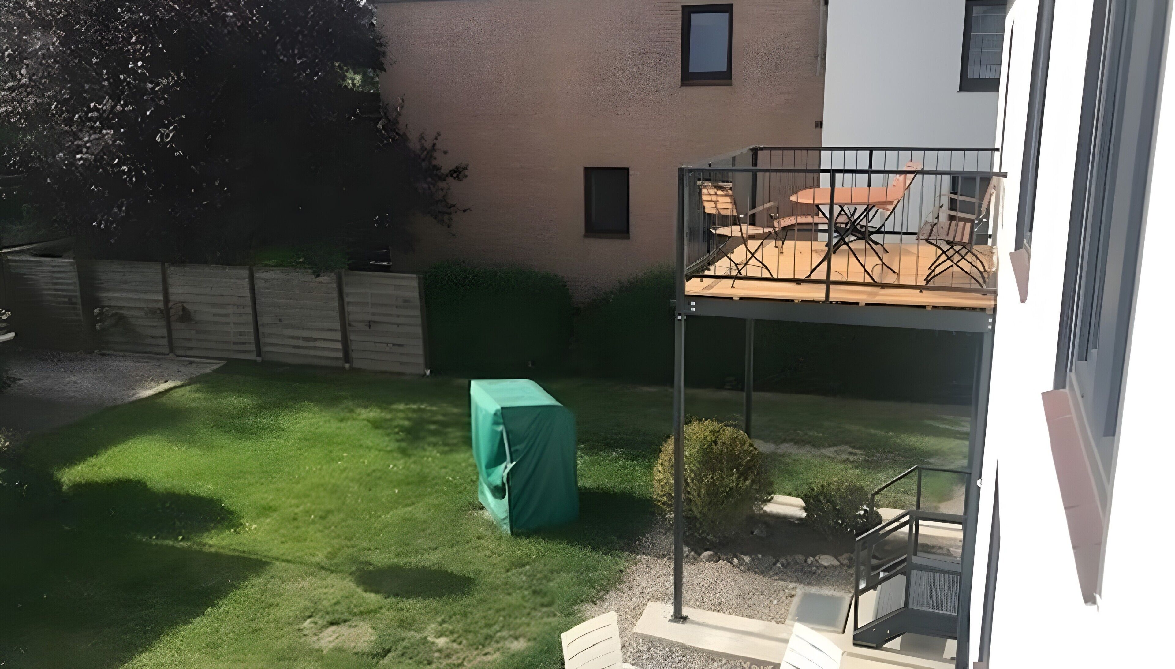 Een achtertuin met gazon, een overdekt object, een patio met stoelen en een trap naar een balkon.