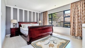 Un dormitorio con una cama grande, dos mesitas de noche, un ventanal con cortinas y vistas a árboles.