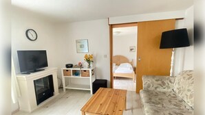 Un soggiorno con televisore, un tavolino in legno, un divano, un mobile TV contenitore e una porta che dà su una camera da letto.