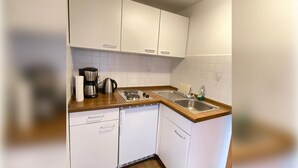 Una cucina compatta con mobili bianchi, una macchina da caffè, un bollitore e un lavello.