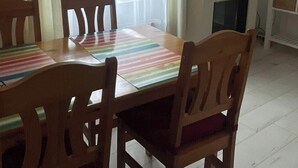 Zona pranzo con tavolo, sedie, lampada a sospensione, televisore e orologio appeso al muro.