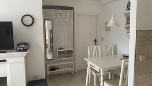 A room with a television, a clock, a mirror, a dining table with chairs, and a hanging light fixture.