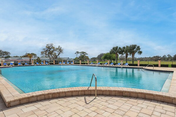 A rectangular swimming pool with a tiled deck, surrounded by lounge chairs and palm trees.