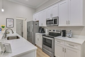 A modern kitchen with white cabinets, stainless steel appliances, and a coffee sign.