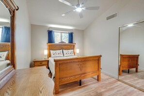 Un dormitorio con cama de madera, mesita de noche, espejo y ventilador de techo.