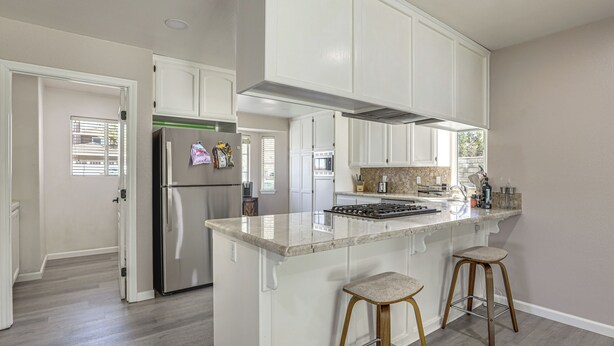 A kitchen with white cabinets, a stainless steel refrigerator, a built-in stove, and two bar stools.