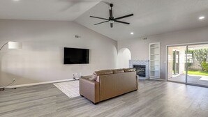 A spacious living room with a large sofa, a flat-screen TV, a ceiling fan, and a fireplace.