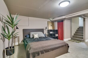Quarto com cama, mesa de cabeceira, luminária, planta em vaso e escada.