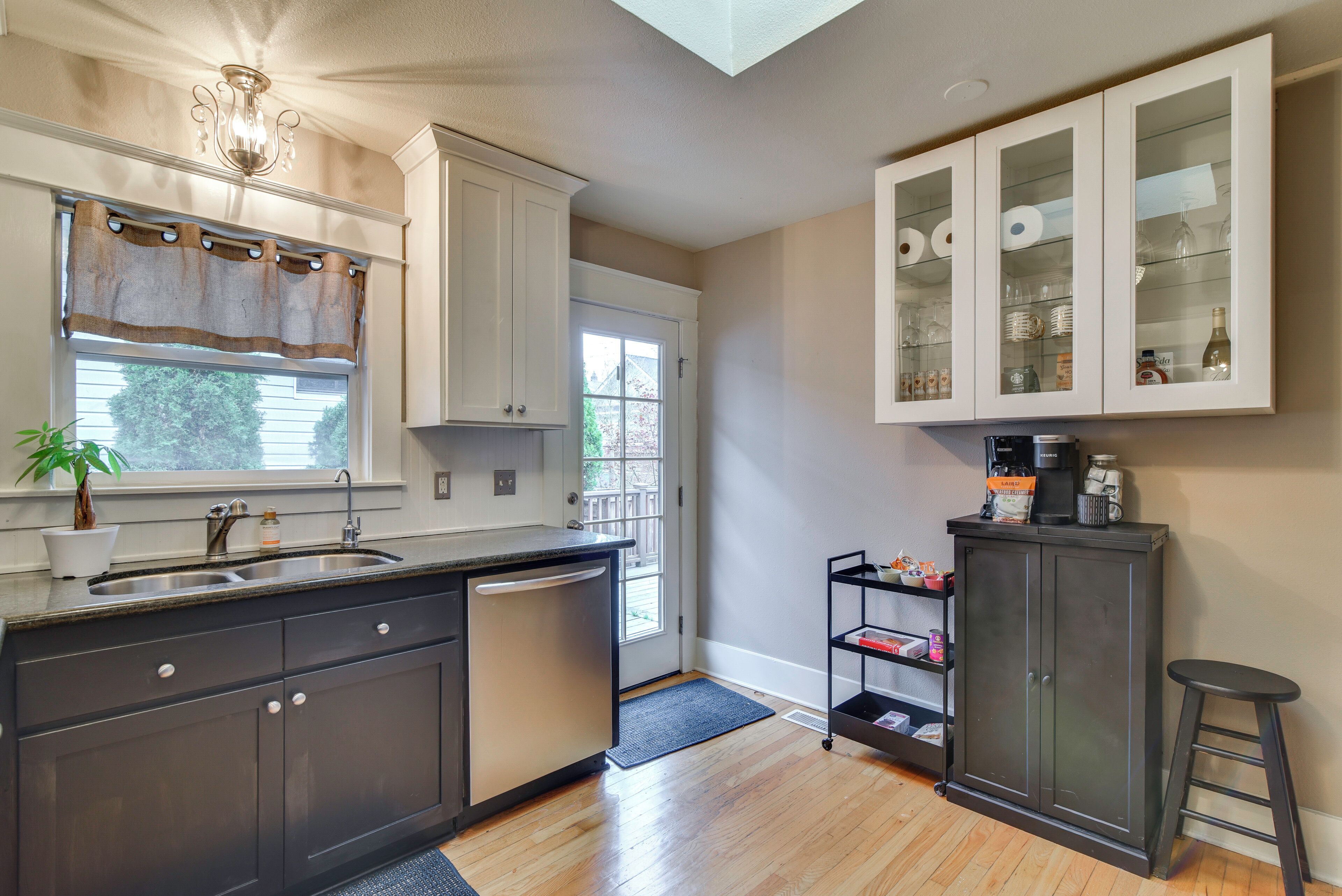 A kitchen with a dishwasher, a sink, a window with curtains, a cabinet with glass doors, and a coffee machine on a shelf.