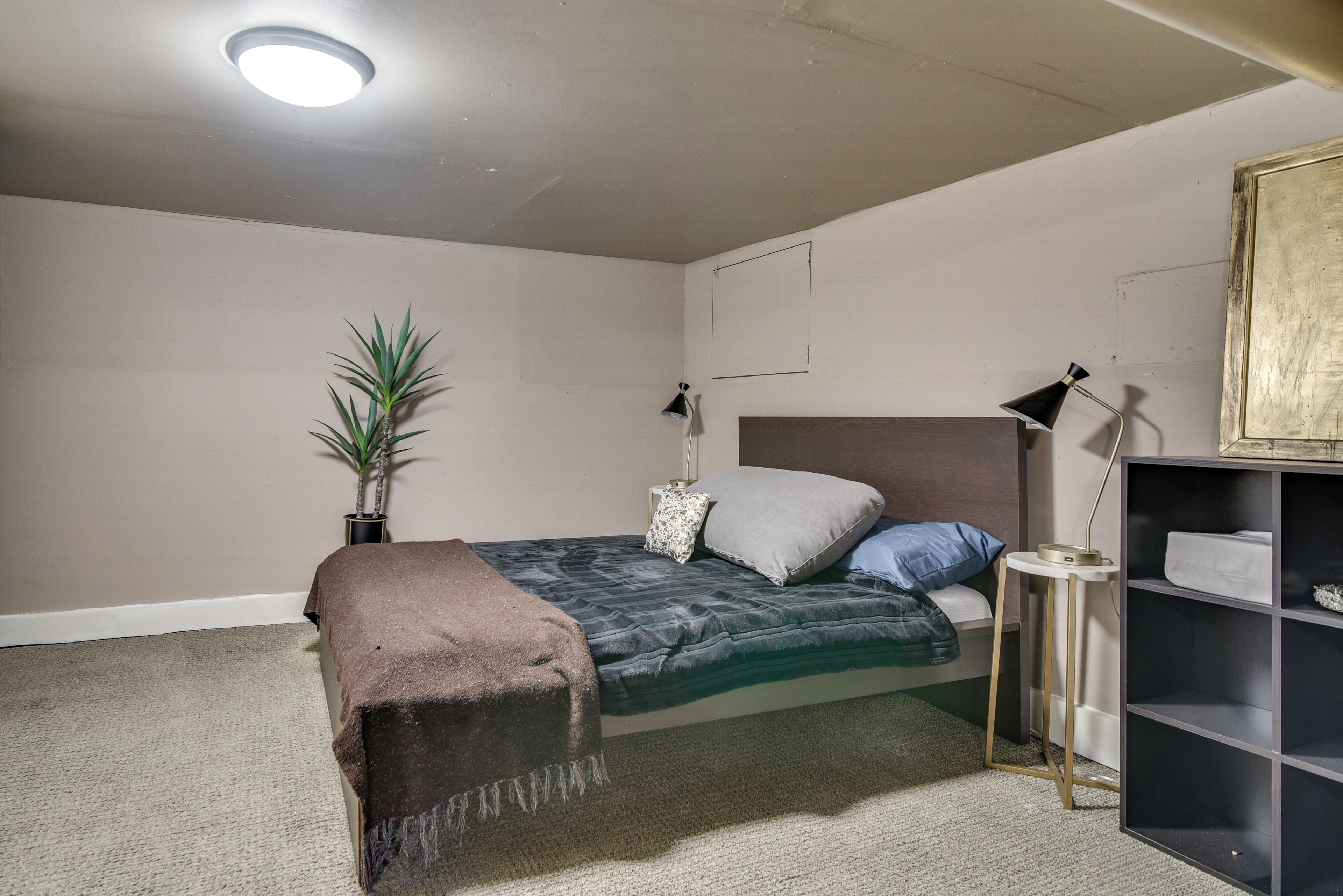 A bedroom with a bed, bedside lamps, a small plant, a bookshelf, and a ceiling light.