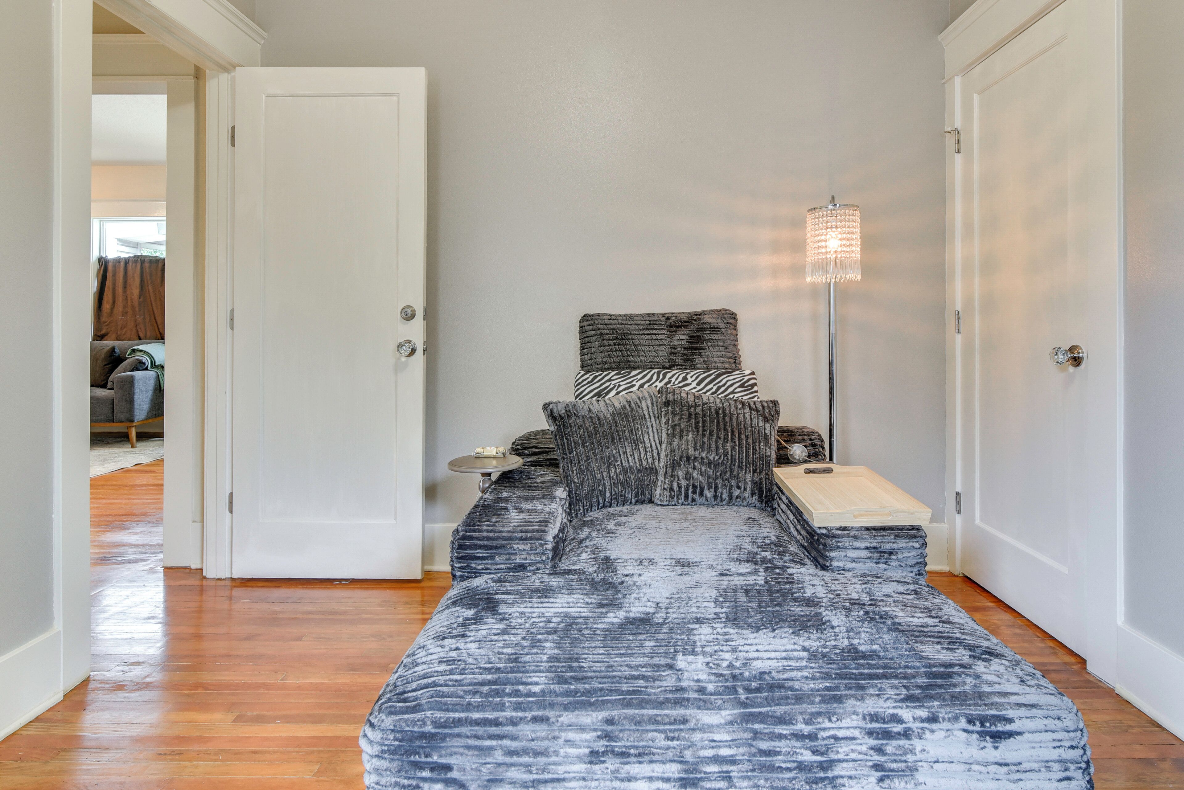 A bedroom with a bed, bedside table, lamp, and a door leading to another room.