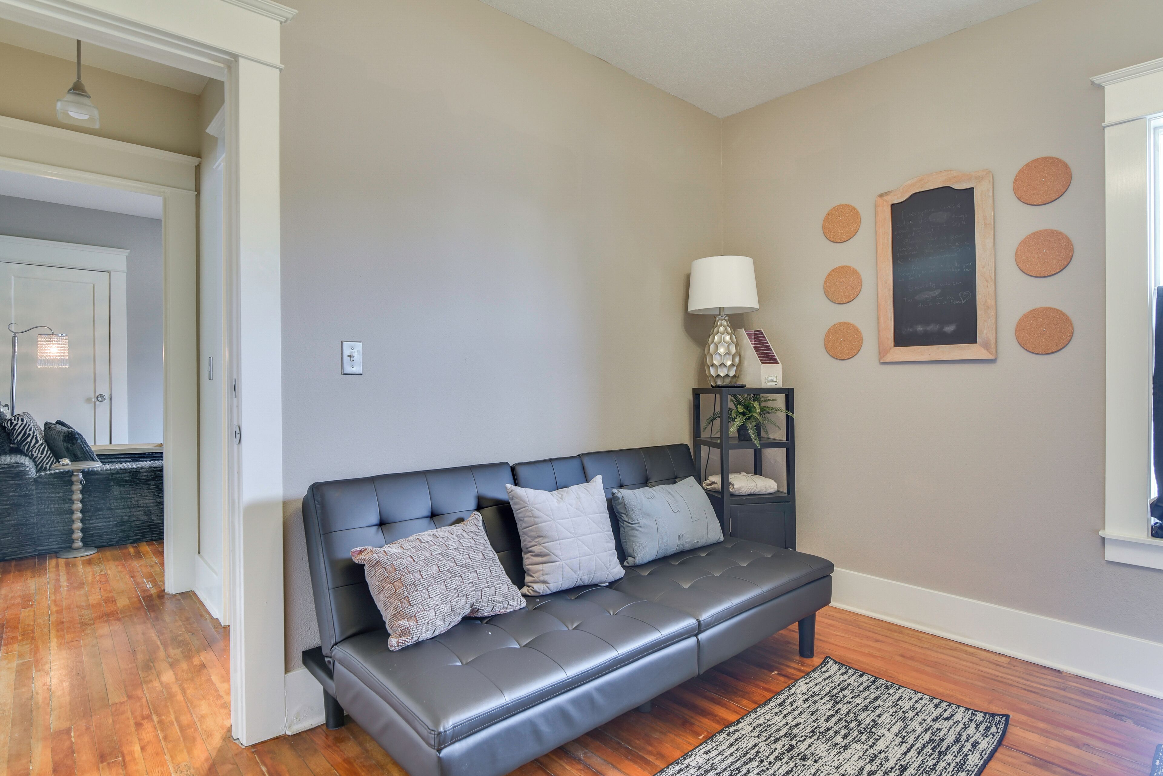 A modern living room with a dark leather sofa, a patterned rug, and a wall-mounted lamp.
