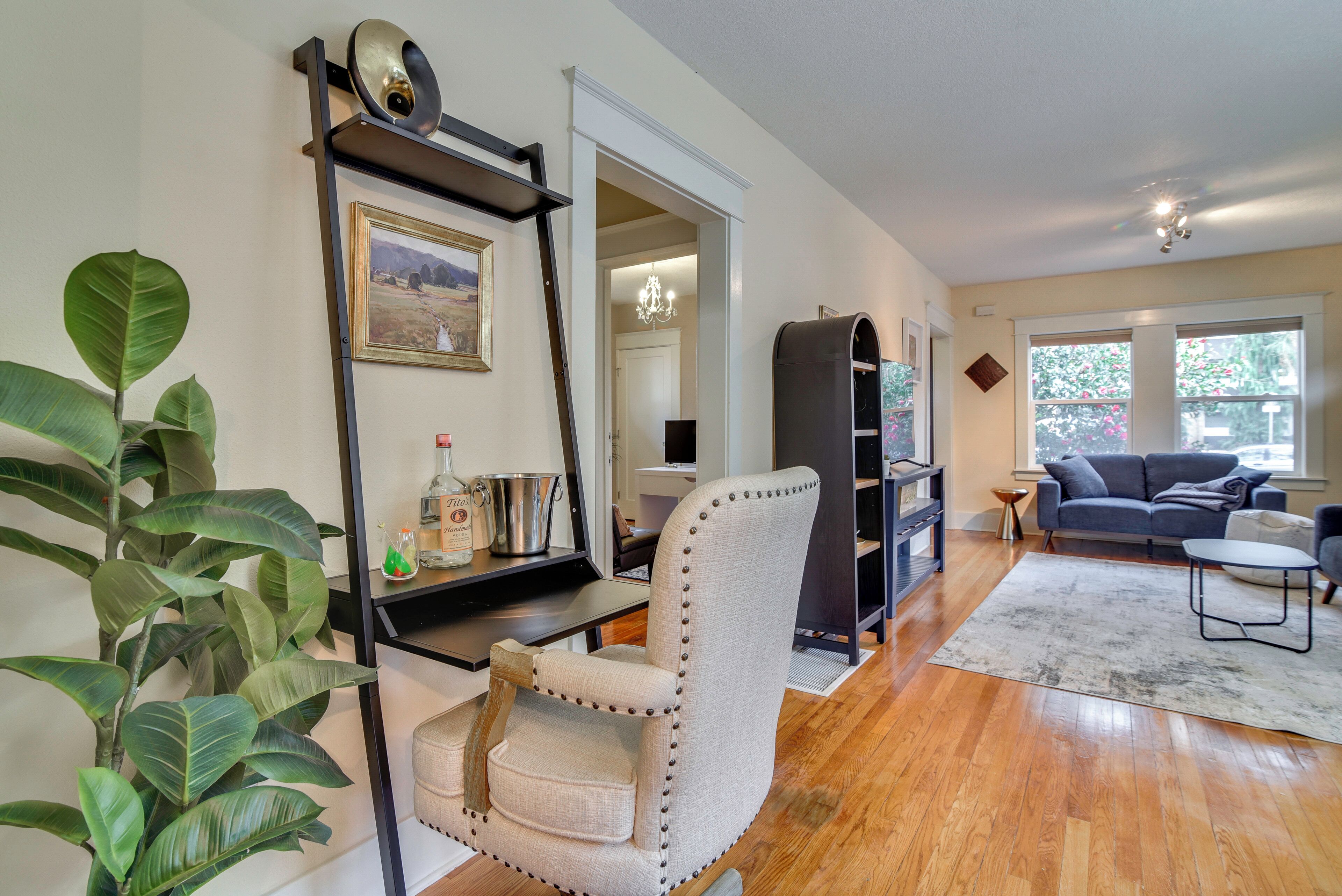 A living room with a wooden floor, a sofa, a chair, a bookshelf, and a potted plant.