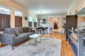 A modern living room with a grey sofa, a small coffee table, and a kitchen area in the background. - Main Street Retreat! Urban Cottage in Vancouver (Vancouver)