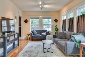 A living room with two sofas, a coffee table, a TV on a stand, and large windows with curtains. - Main Street Retreat! Urban Cottage in Vancouver (Vancouver)