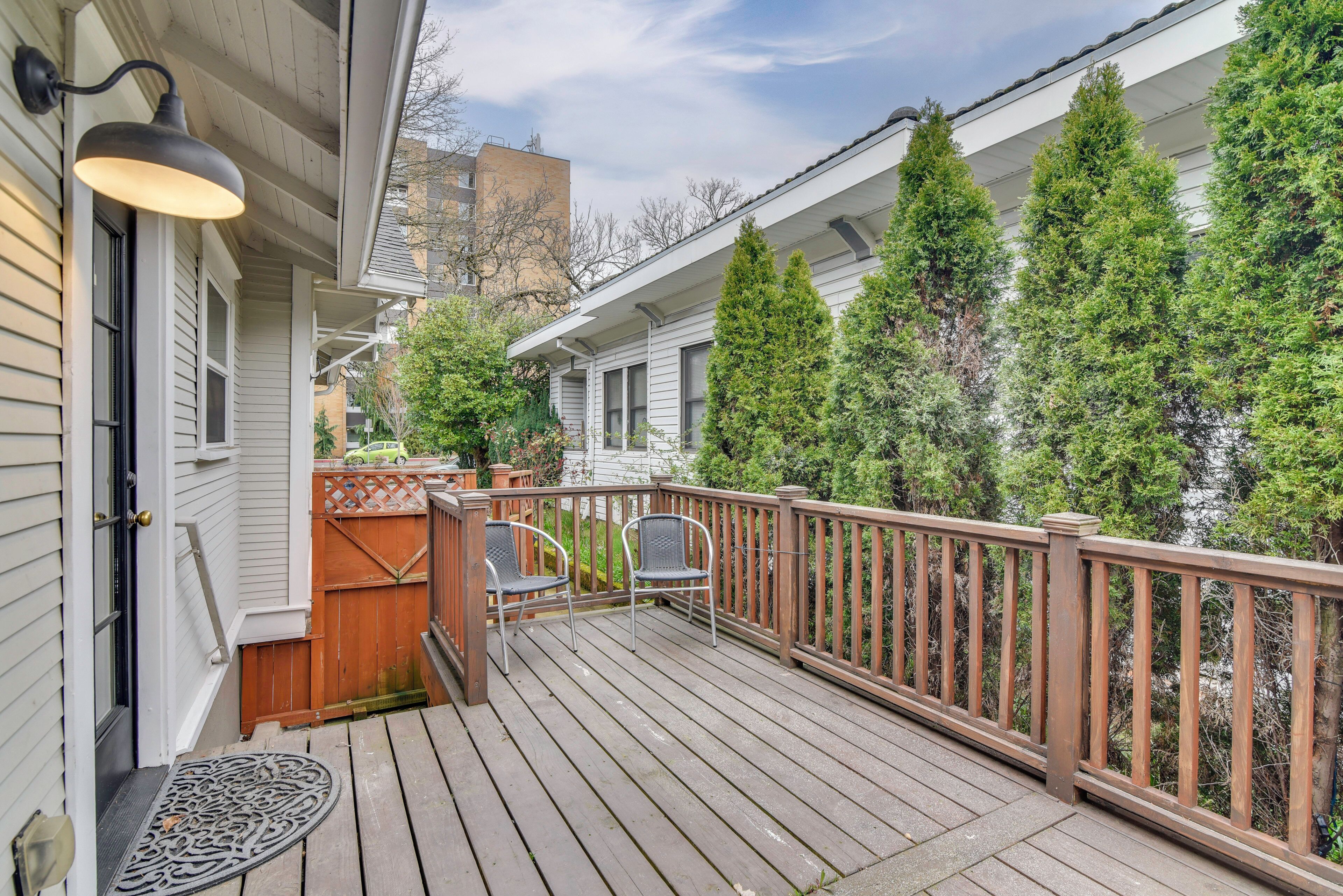 A wooden deck with a railing, two chairs, and a door with a light fixture.