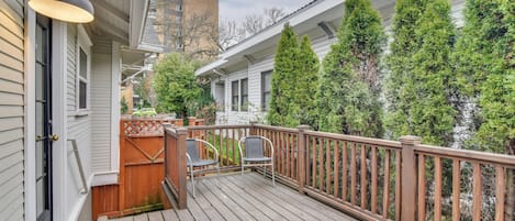 A wooden deck with a railing, two chairs, and a door with a light fixture.