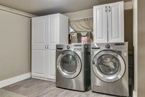 A laundry room with two front-loading washing machines, a cabinet, and a window with a curtain. - Main Street Retreat! Urban Cottage in Vancouver (Vancouver)
