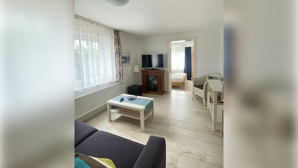 Un salon avec un canapé, une table basse, un téléviseur et un lit à l’arrière-plan.