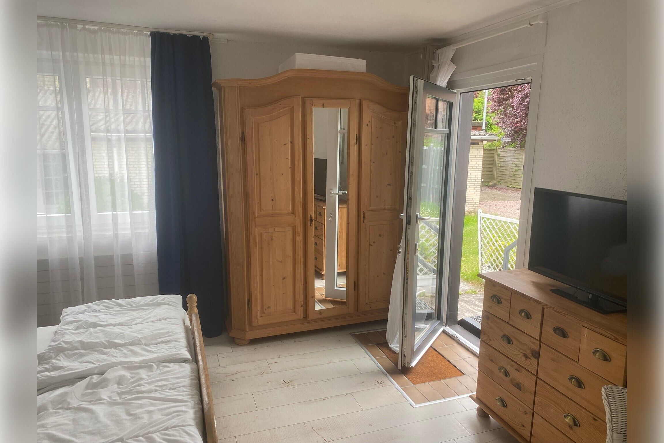 Ein Schlafzimmer mit einem Bett, einem Holzschrank, einem TV-Schrank und einer Glastür zum Balkon.