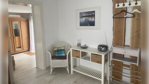 Une pièce avec un bureau blanc, une chaise en osier, un tableau accroché au mur et un porte-manteau.