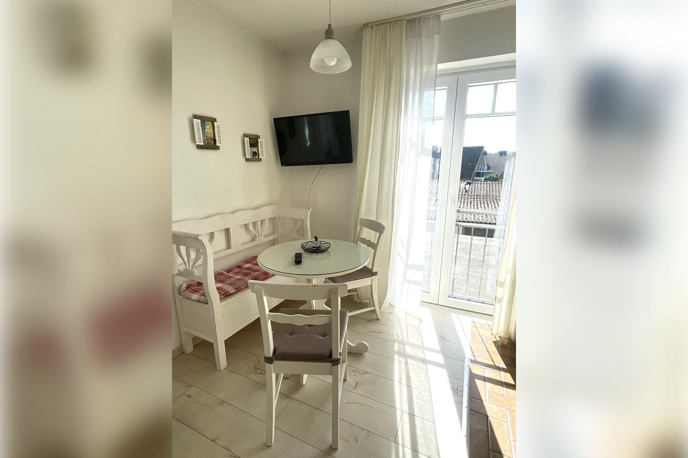 Ein Zimmer mit einem weißen Sofa, einem runden Tisch, einem an der Wand montierten Fernseher und einem Balkon mit Blick.