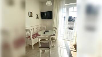 Ein Zimmer mit einem weißen Sofa, einem runden Tisch, einem an der Wand montierten Fernseher und einem Balkon mit Blick.