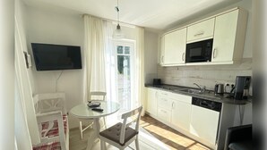Cocina compacta con armarios blancos, microondas, cafetera y comedor con mesa y sillas.