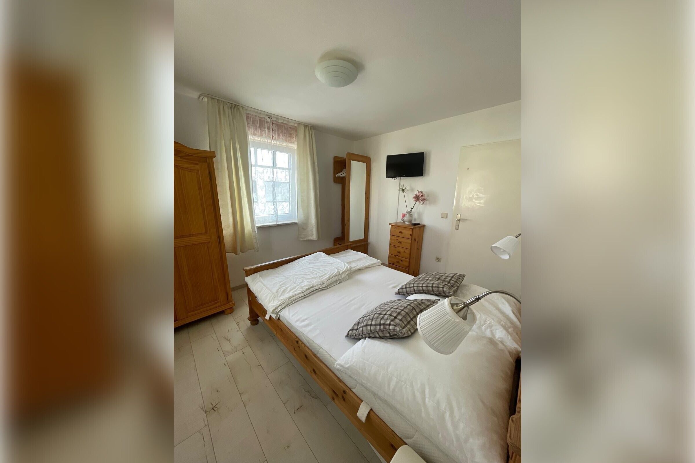 Ein Schlafzimmer mit einem Holzbett, einem Kleiderschrank, einem Spiegel, einem Fernseher und einer Nachttischlampe.