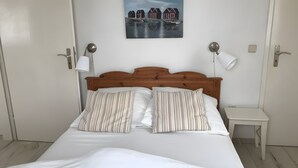 Una cama bien hecha con almohadas a rayas, un cabecero de madera y una mesita de noche con una lámpara.
