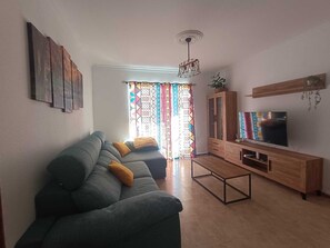Ein Wohnzimmer mit einer Couch, einem Fernseher, einer Holzkabine und gemusterten Vorhängen.