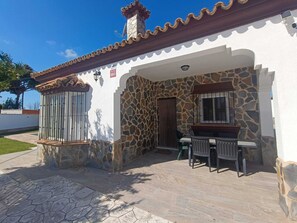 Ein Haus mit einer Steinaußenfassade, einer gefliesten Terrasse und einem Essbereich mit Stühlen und einem Tisch.