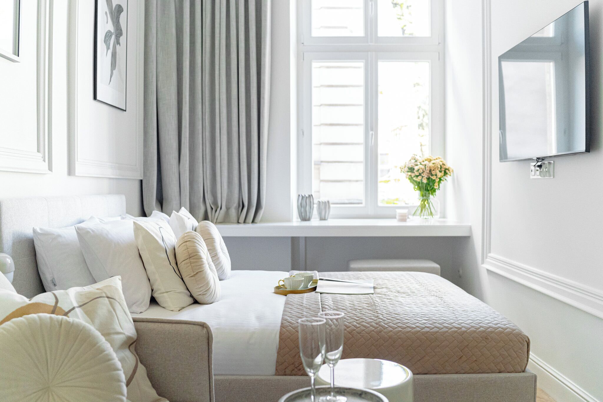 A hotel room with a bed, a bedside table, a TV, a window with curtains, and a view of the outside.