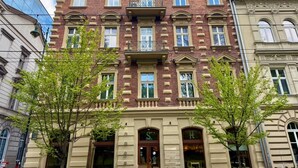 Un immeuble à plusieurs étages, de style architectural classique, doté d’un balcon central orné de balustrades travaillées, de grandes fenêtres et d’une entrée au niveau du sol avec une enseigne.