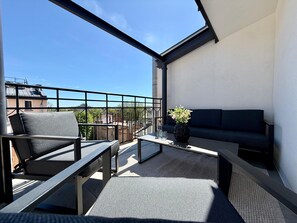 Ein Balkon mit einer Couch, Stühlen, einem Tisch und einem Blumentopf.