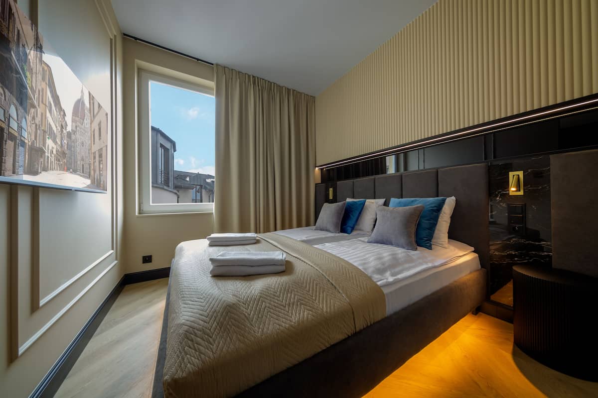 Una habitación de hotel moderna con una cama grande, una ventana con cortinas, un cabecero y una mesita de noche.