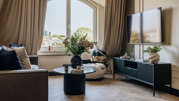 Un salon avec un canapé, une table basse ronde, un téléviseur et une fenêtre avec des rideaux.