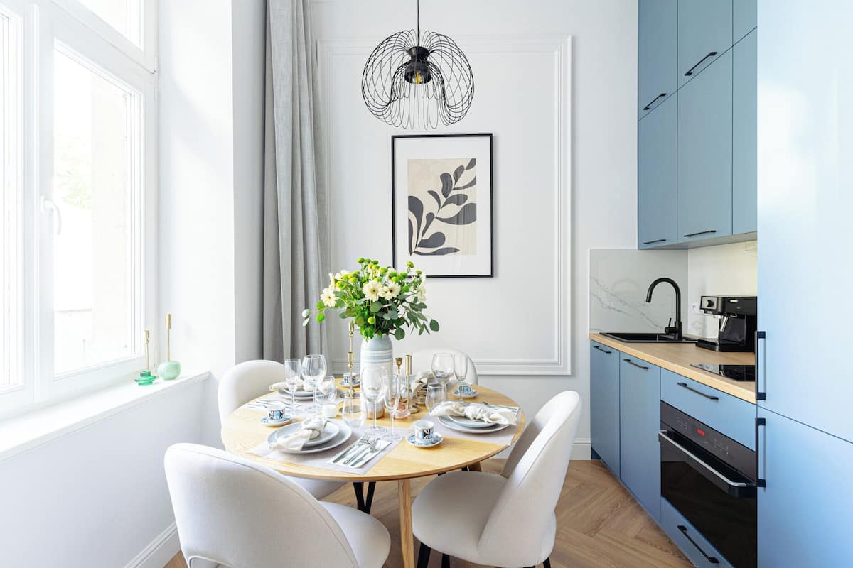 Un comedor con una mesa redonda dispuesta para cuatro, un jarrón con flores y una obra de arte enmarcada en la pared.